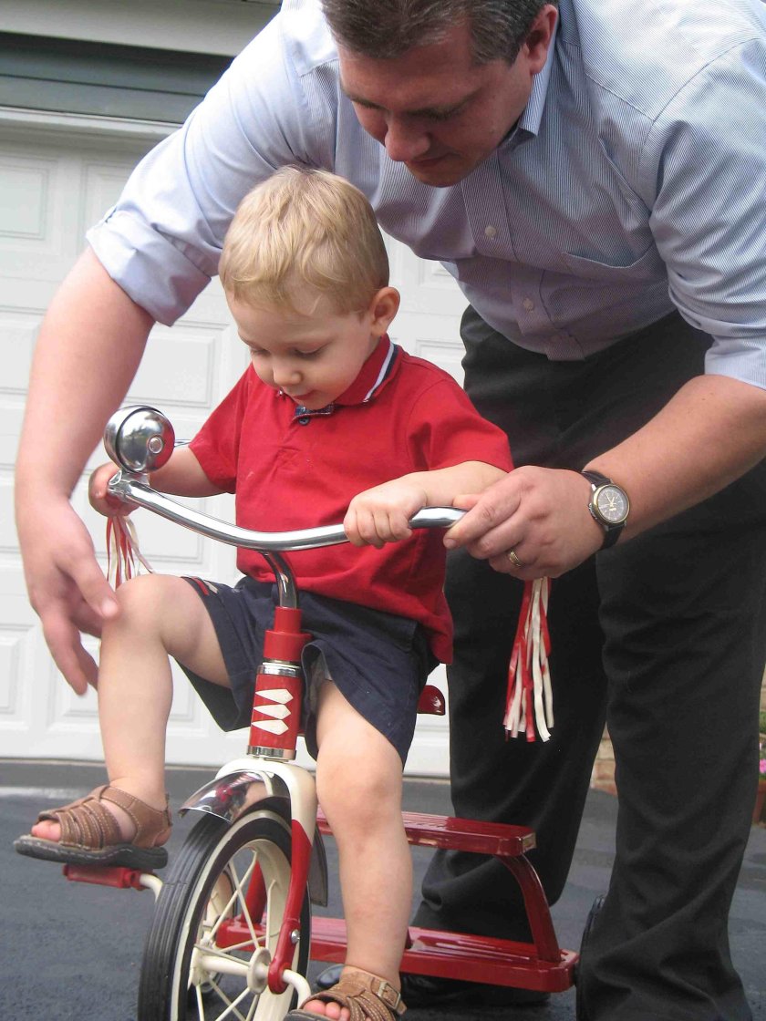 Мама учит ребёнка кататься на трехколесном велосипеде фото